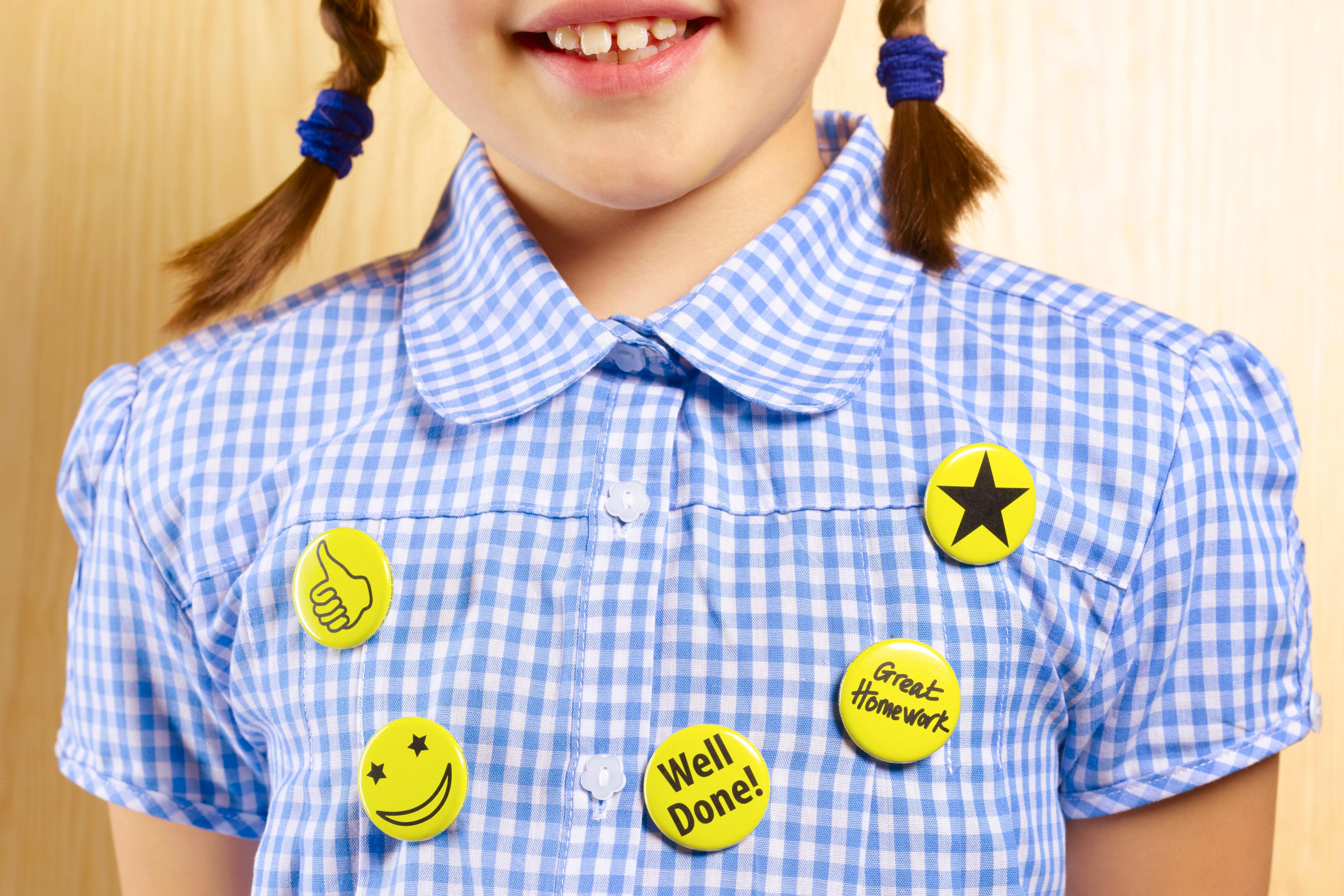 Photo of a child in a blue gingham shirt with yellow badges featuring positive messages and symbols on the chest.