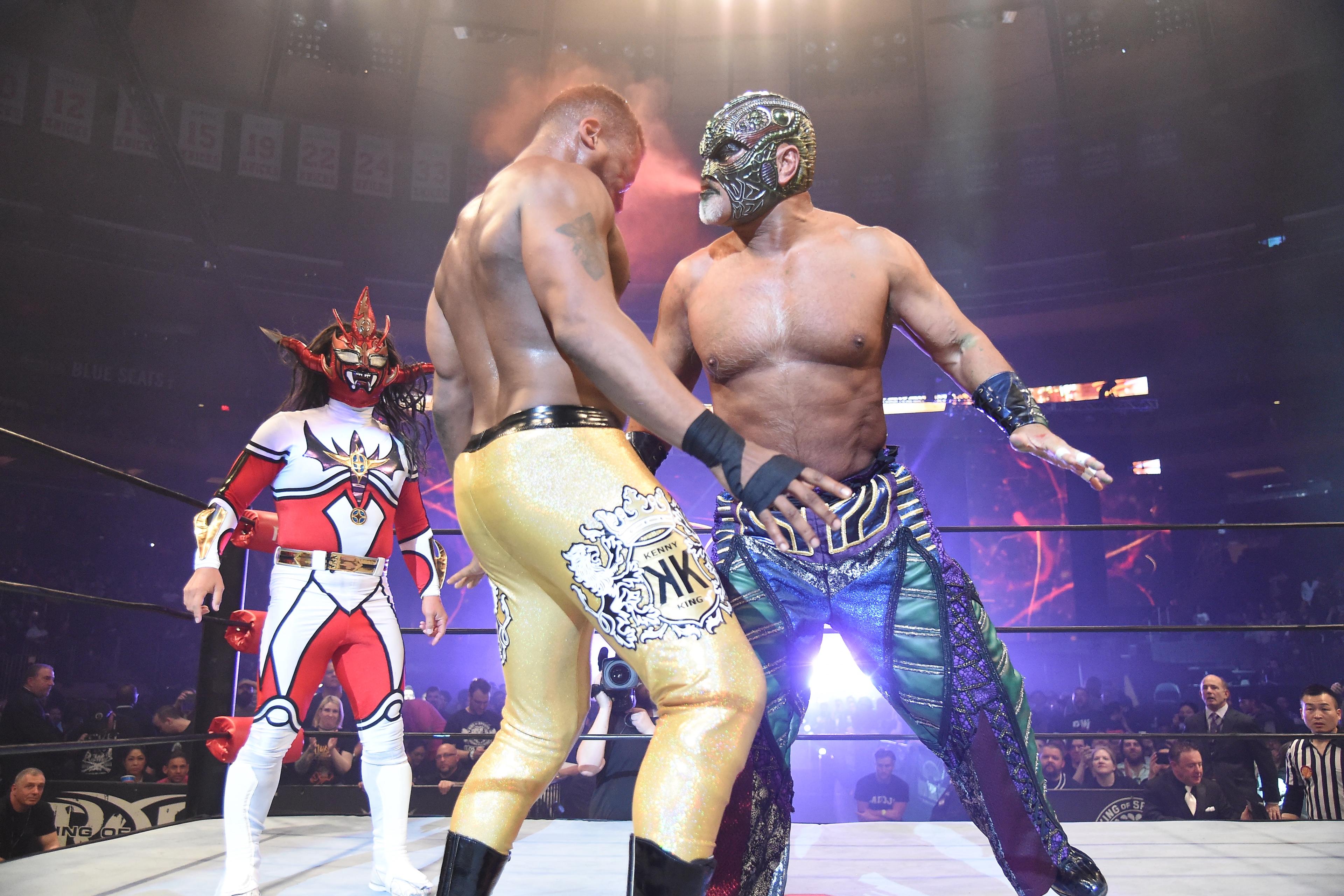 Photo of masked wrestlers in a ring, one in bright red and white, another in gold trousers, with a cheering crowd.