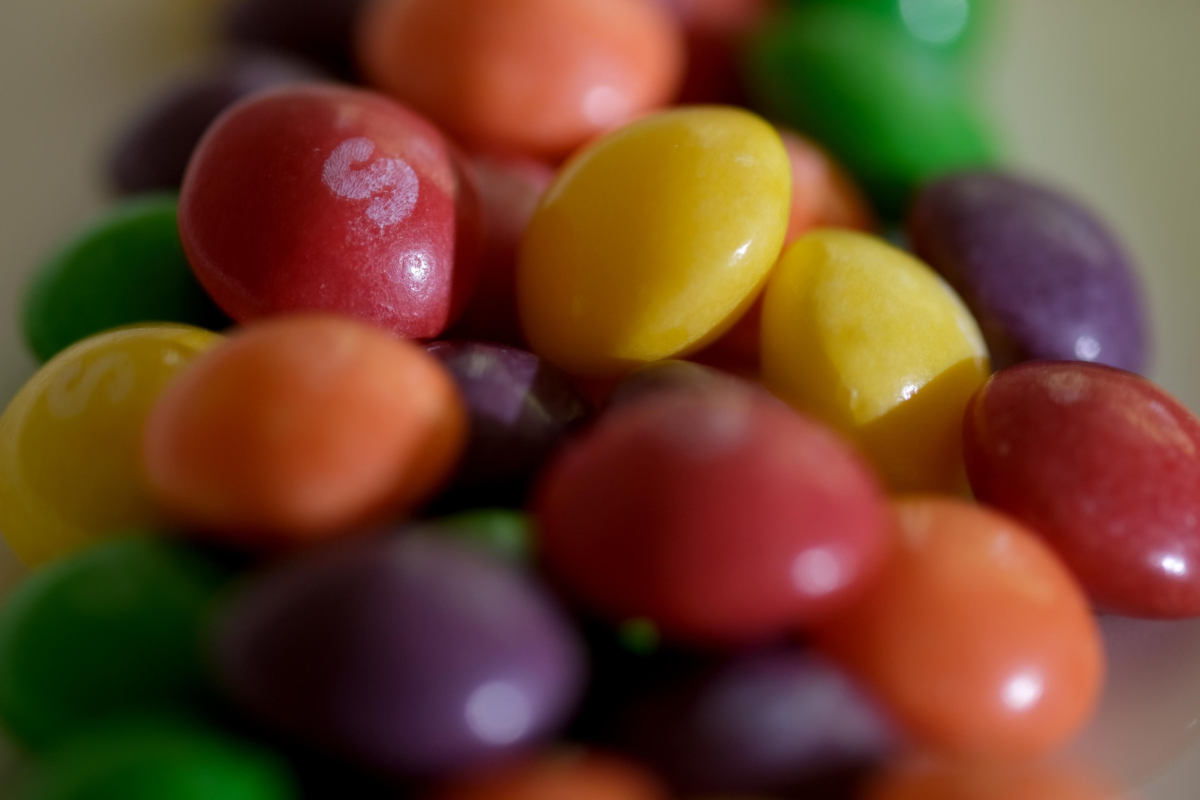 Photo of colourful candy close-up with red, yellow, green and purple pieces, some marked with a white “S”.
