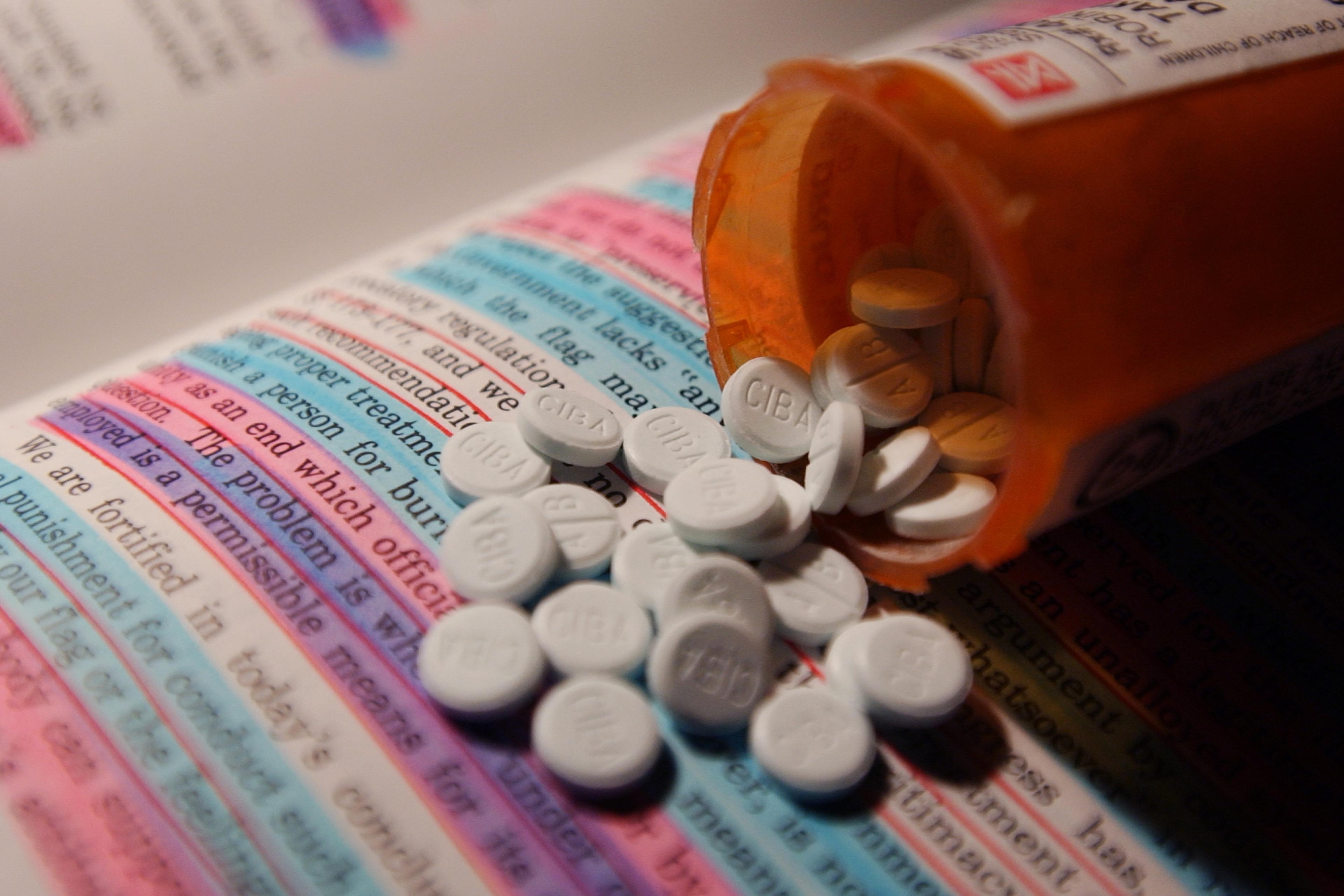 A prescription pill bottle spilling tablets onto an open book with highlighted text.