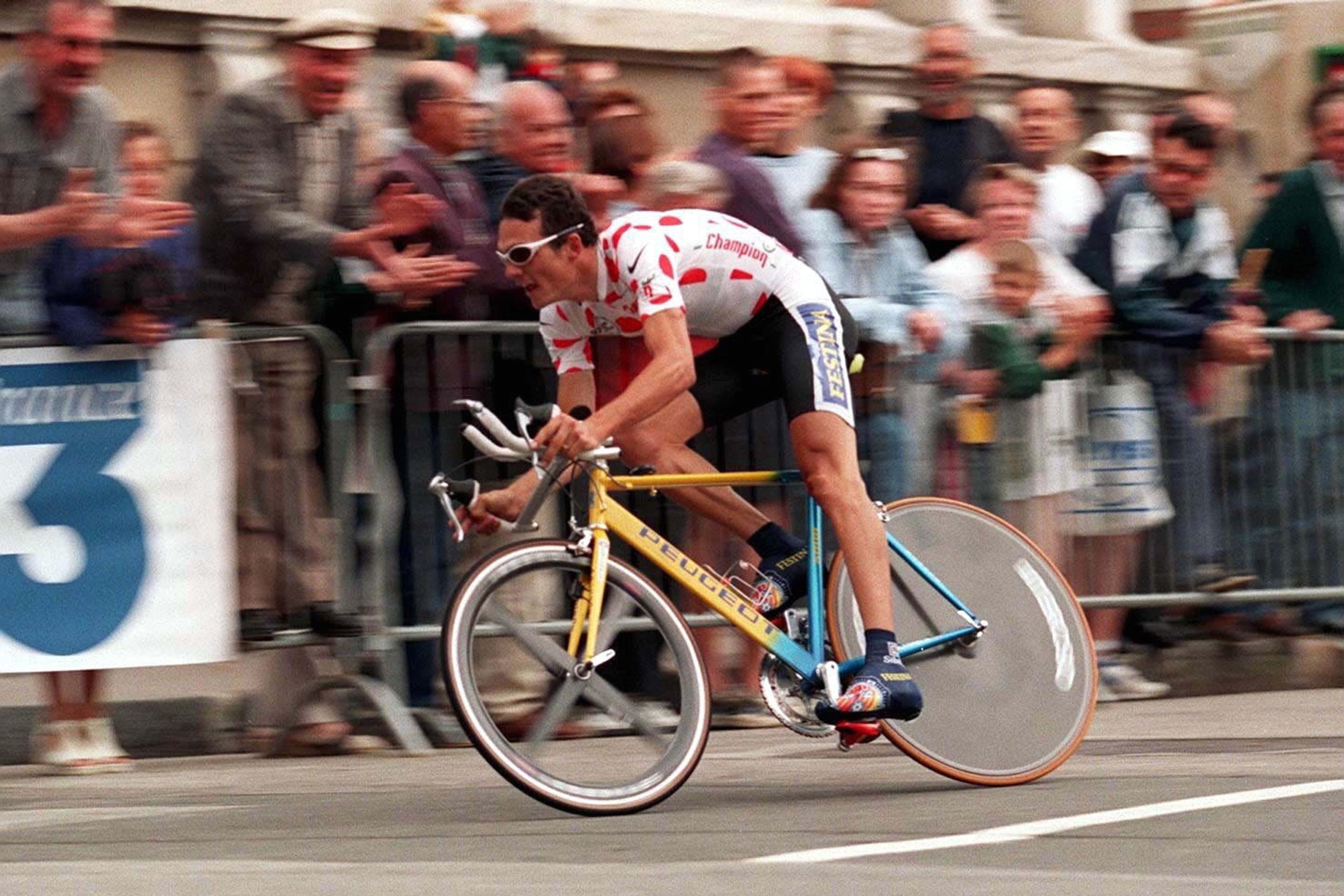Photo of a cyclist in a red polka dot jersey racing past a cheering crowd on a yellow bicycle.