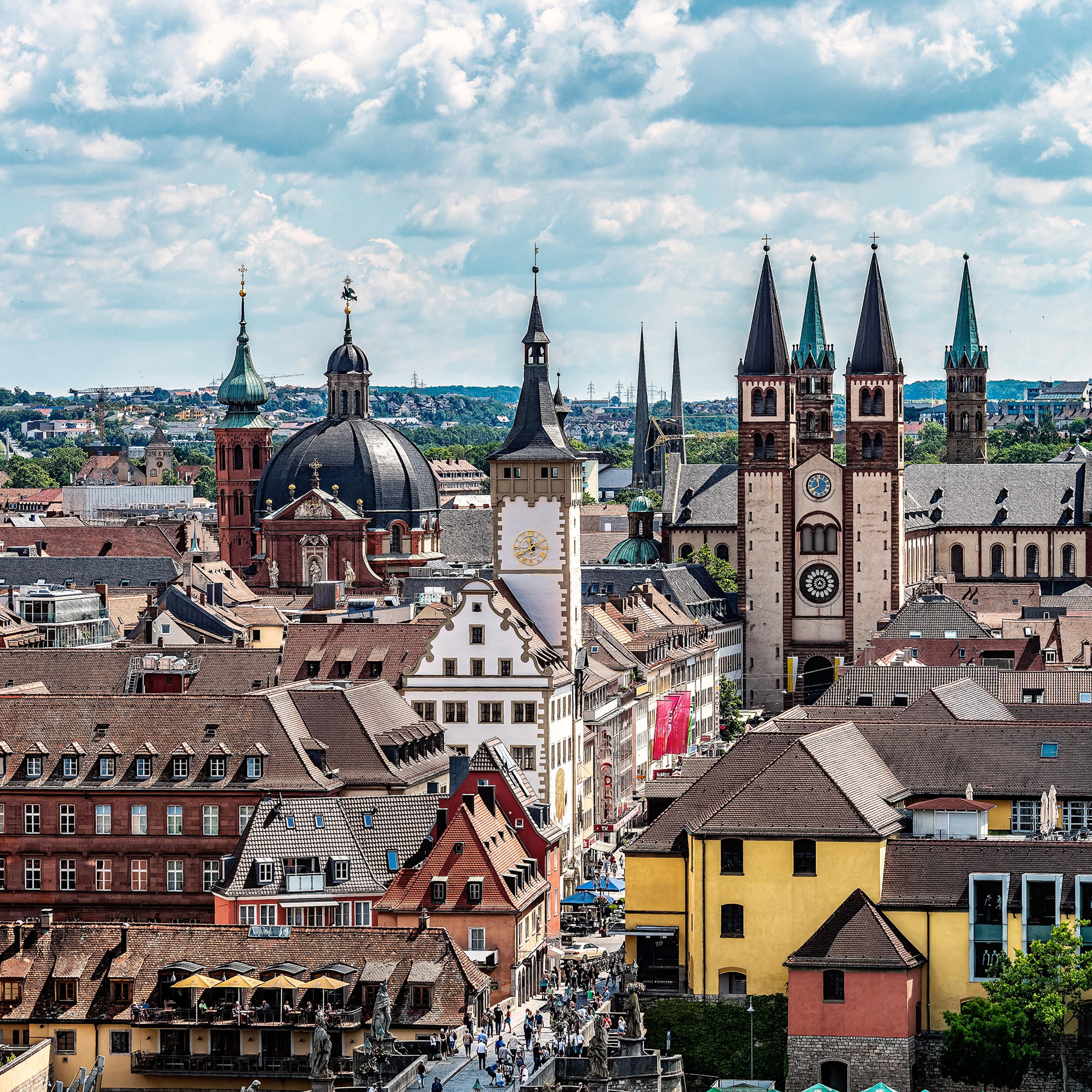 Aerial photo of Würzburg, a European cityscape with historic buildings, church spires and a clock tower under a partly cloudy sky.