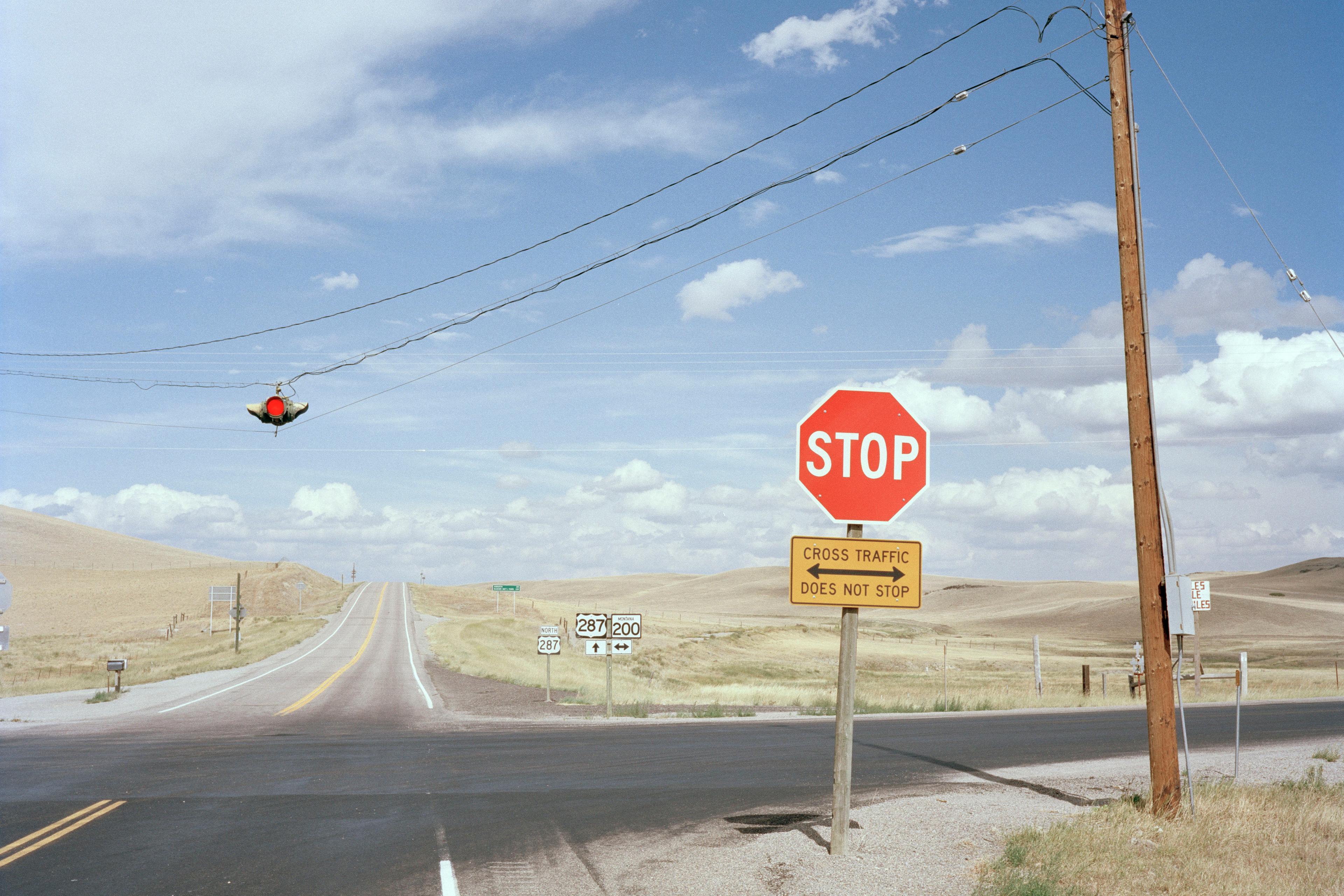 A rural road intersection with a stop sign, traffic light and highway signs under a blue sky with clouds.