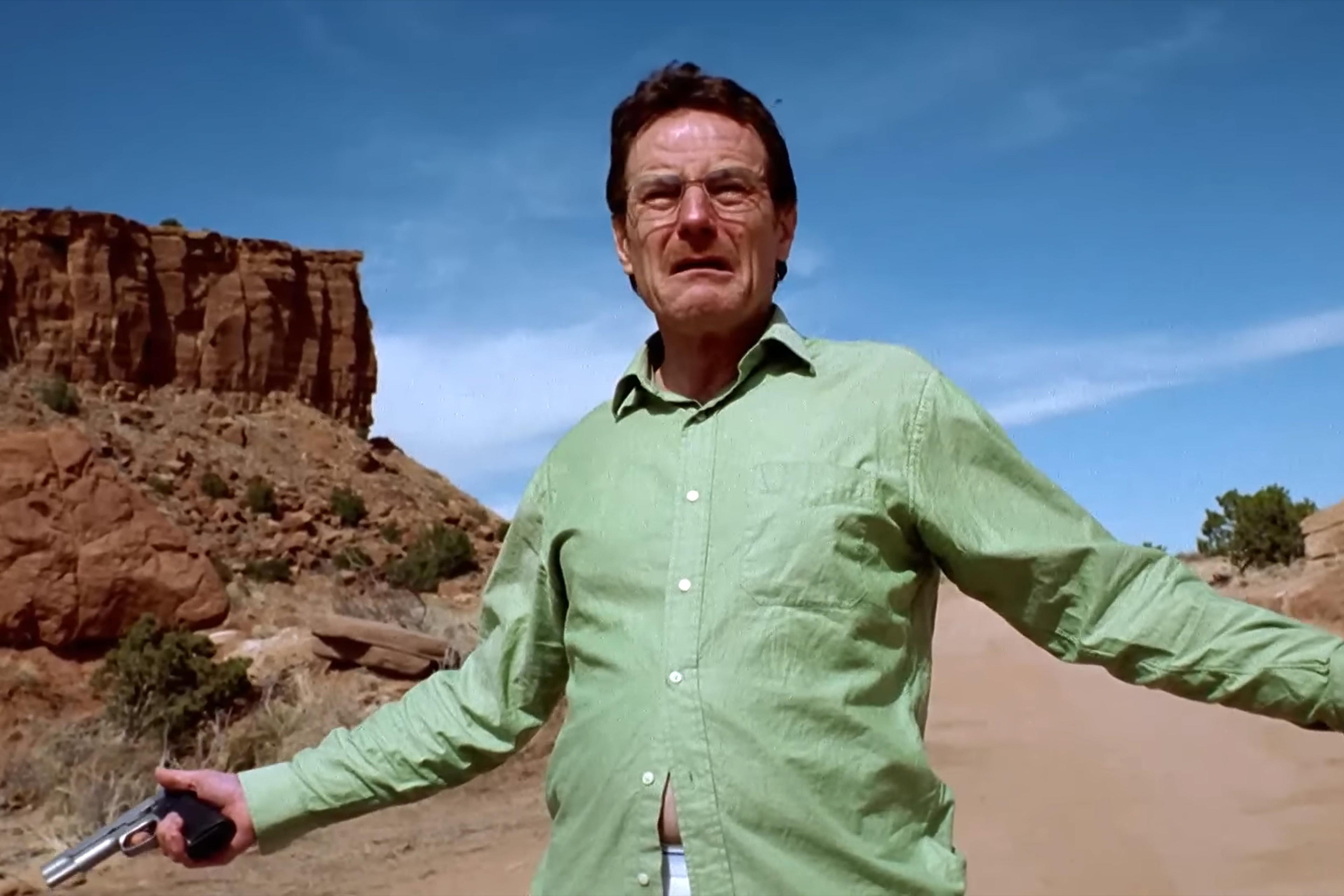 Photo of a man in a green shirt holding a gun in a desert landscape with rocky cliffs under a blue sky.