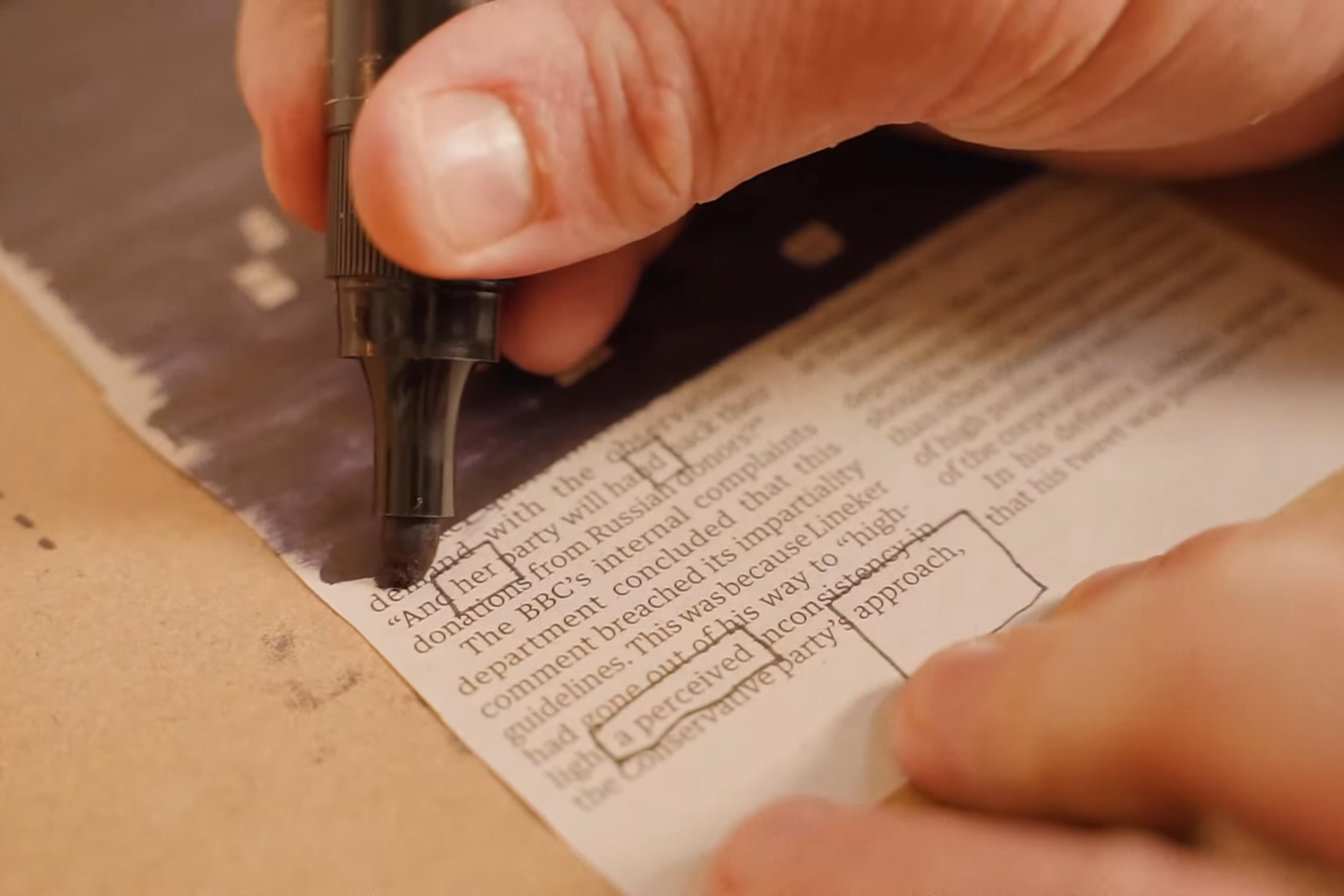 Photo of a hand using a black marker to redact text on paper several words are boxed to be emphasised.