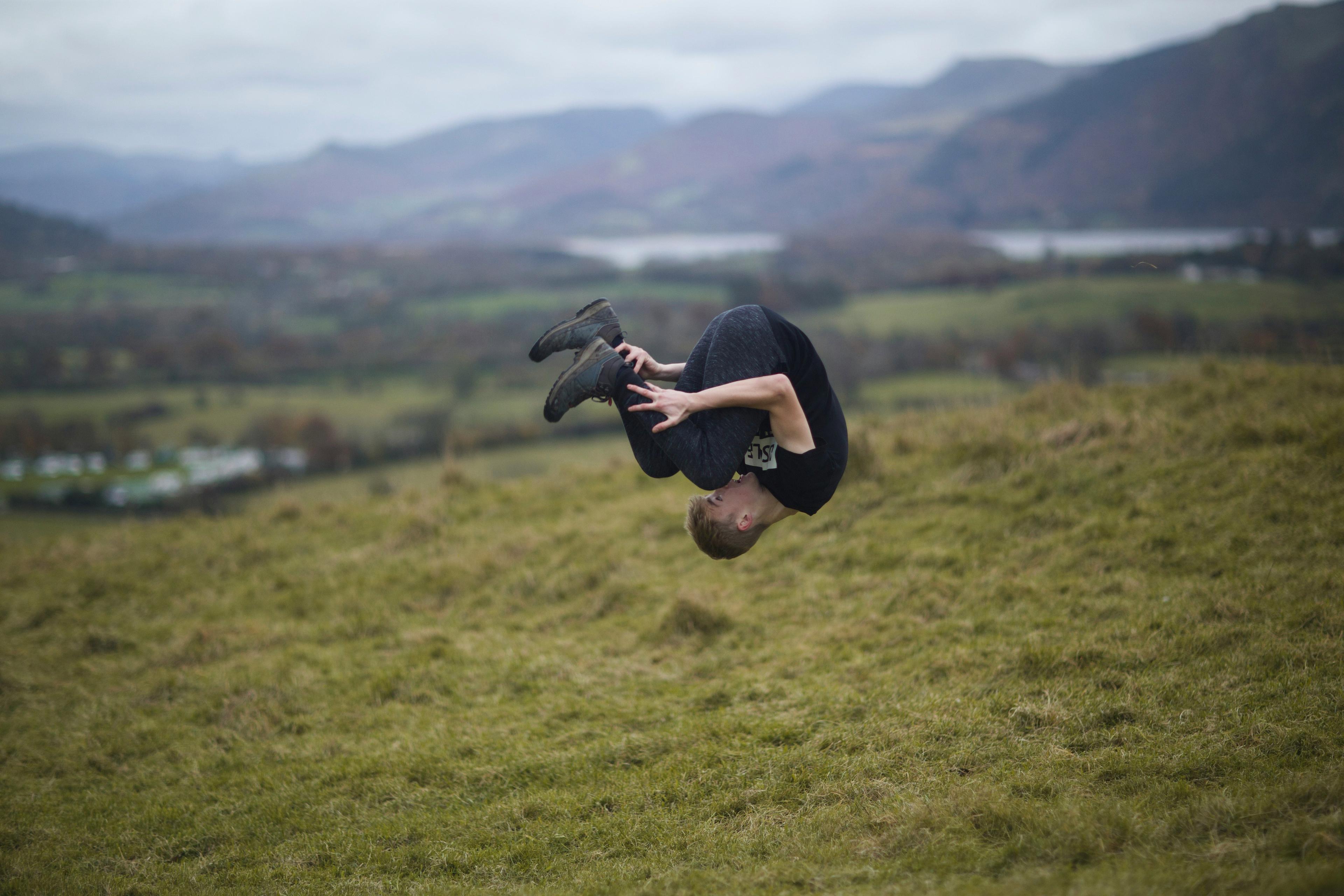A person in the air, mid-flip, on a grassy hill with distant hills in the background.