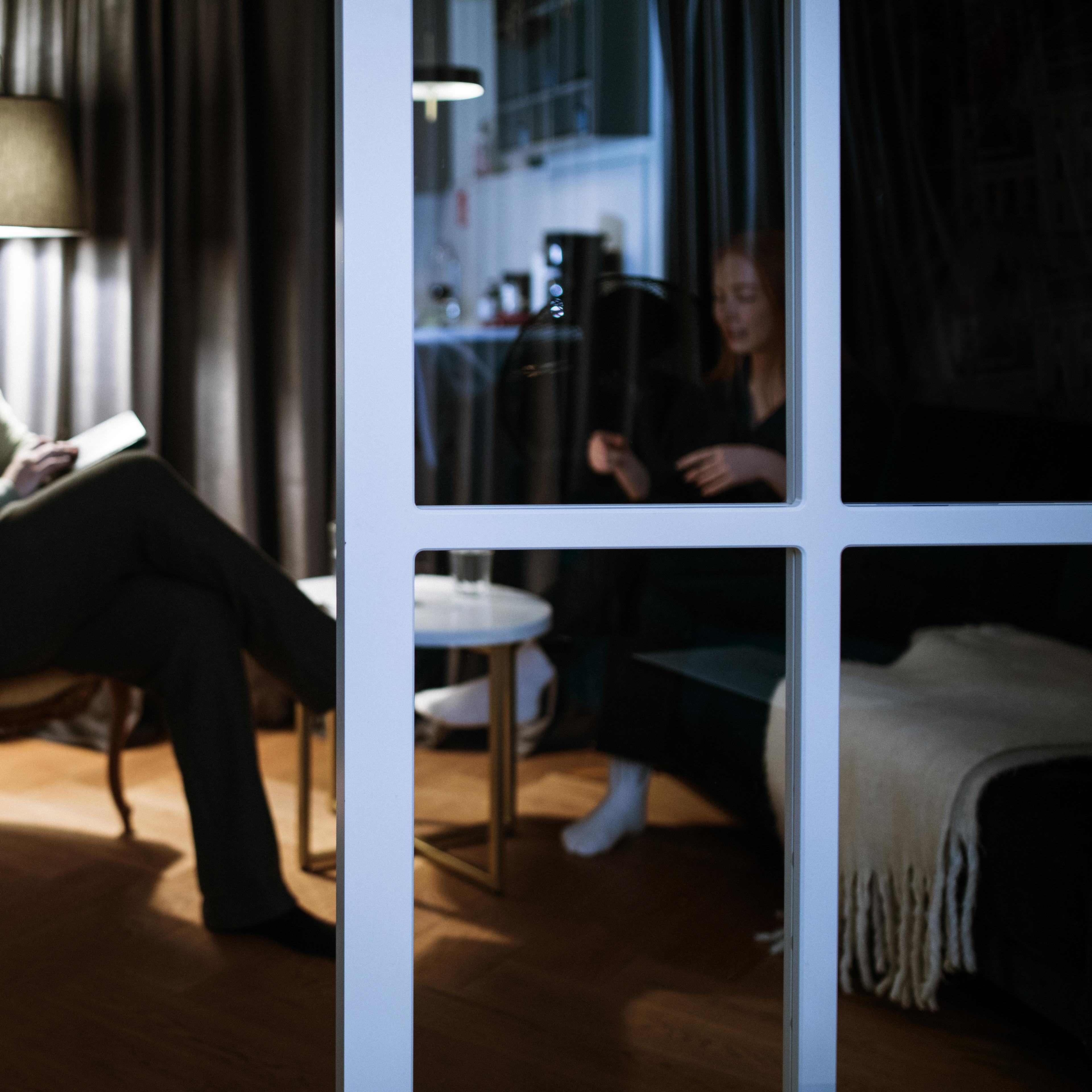 A man holding a notepad and a woman talking in a dimly lit room seen through glass doors.