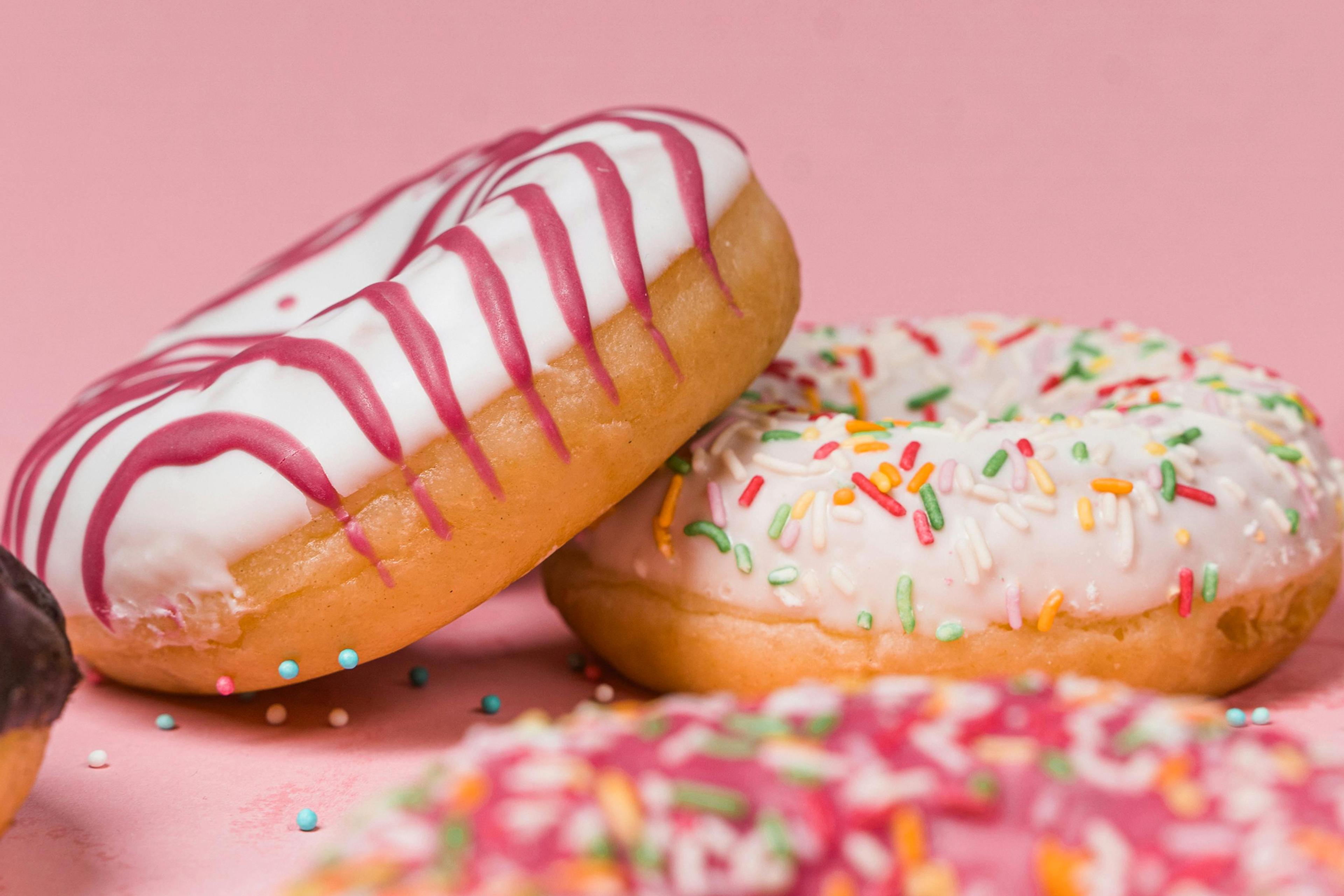 Photo of doughnuts with white icing and colourful sprinkles on a pink background.