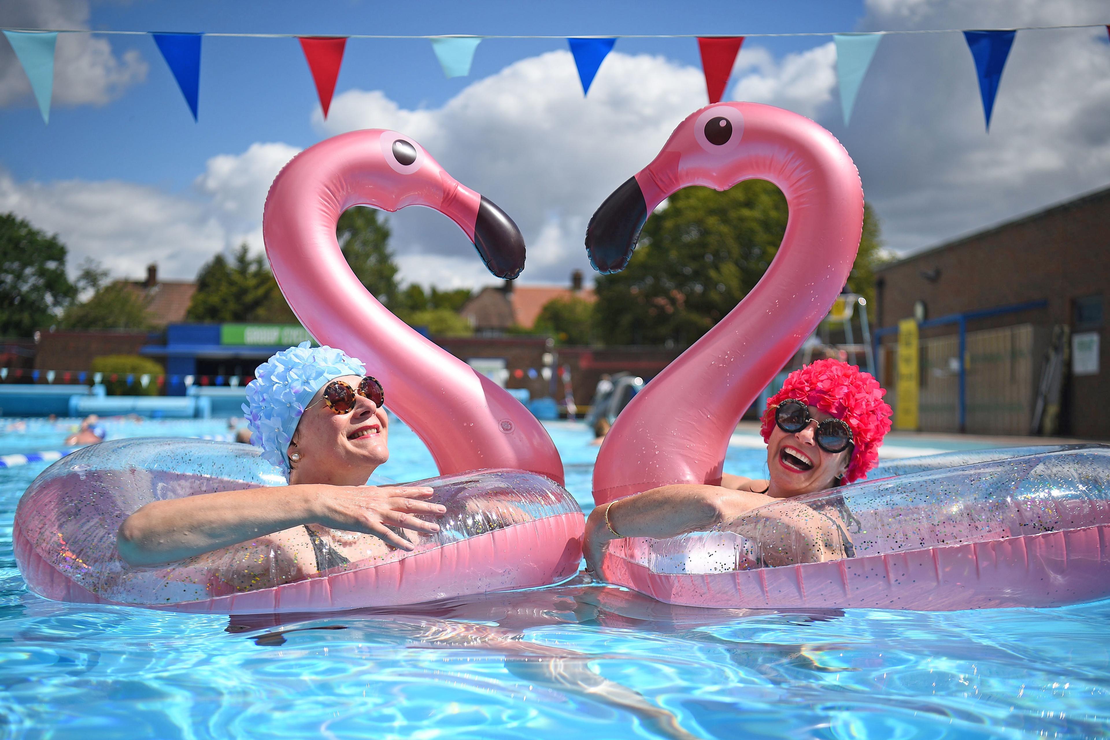 Photo of two people in a pool, wearing floral swim caps using inflatable pink flamingo rings, with bunting overhead.