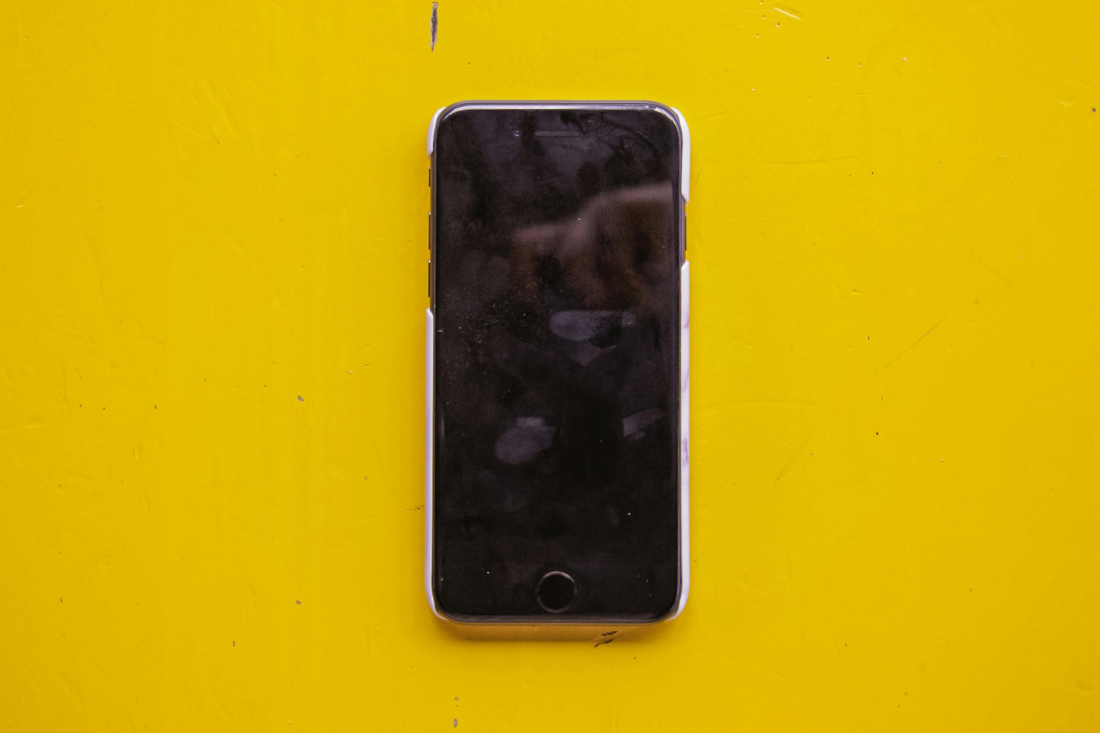 A switched-off smartphone on a bright yellow surface with fingerprints and smudges on the black screen.
