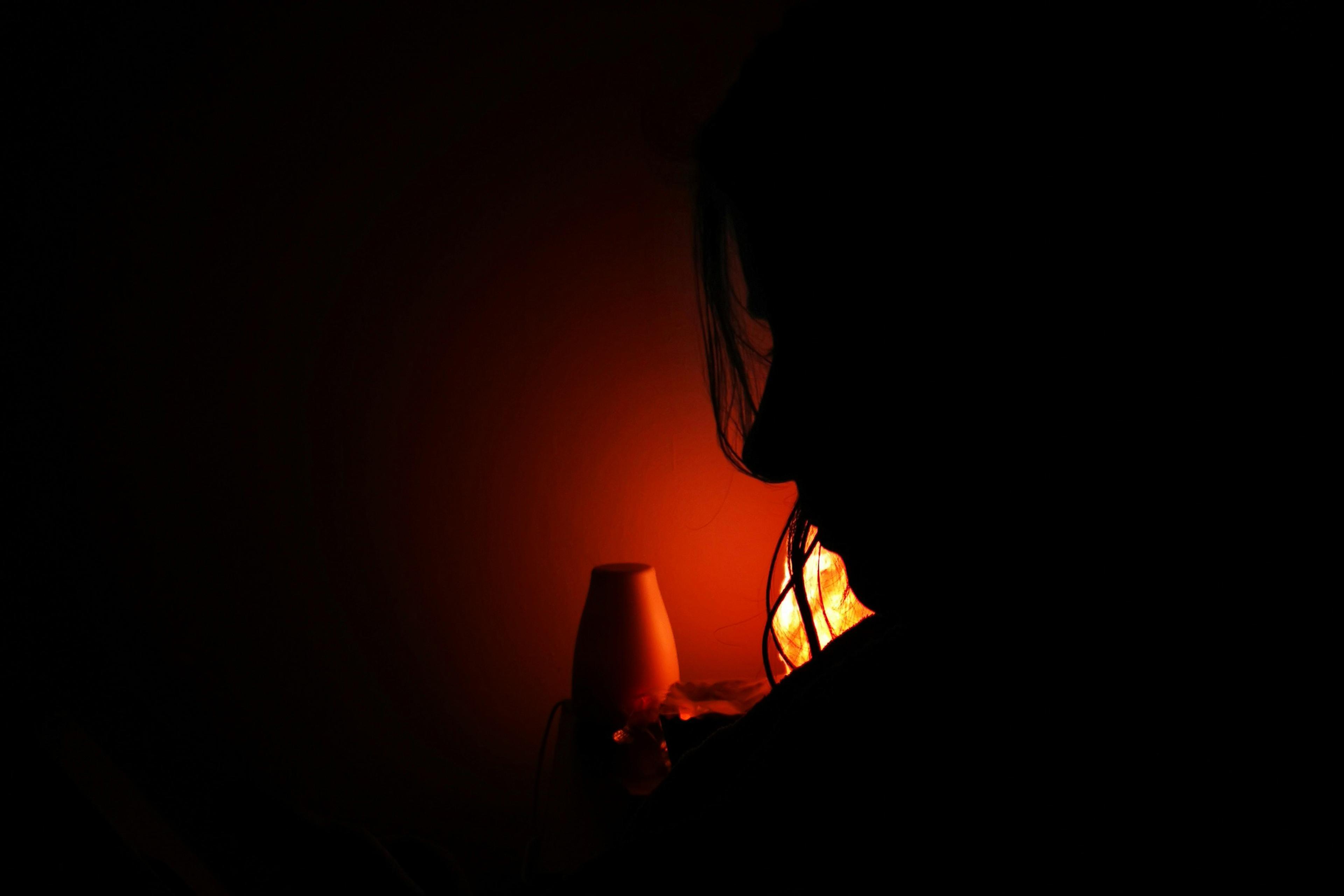 Silhouette of a person next to a glowing orange lamp in a dark room.