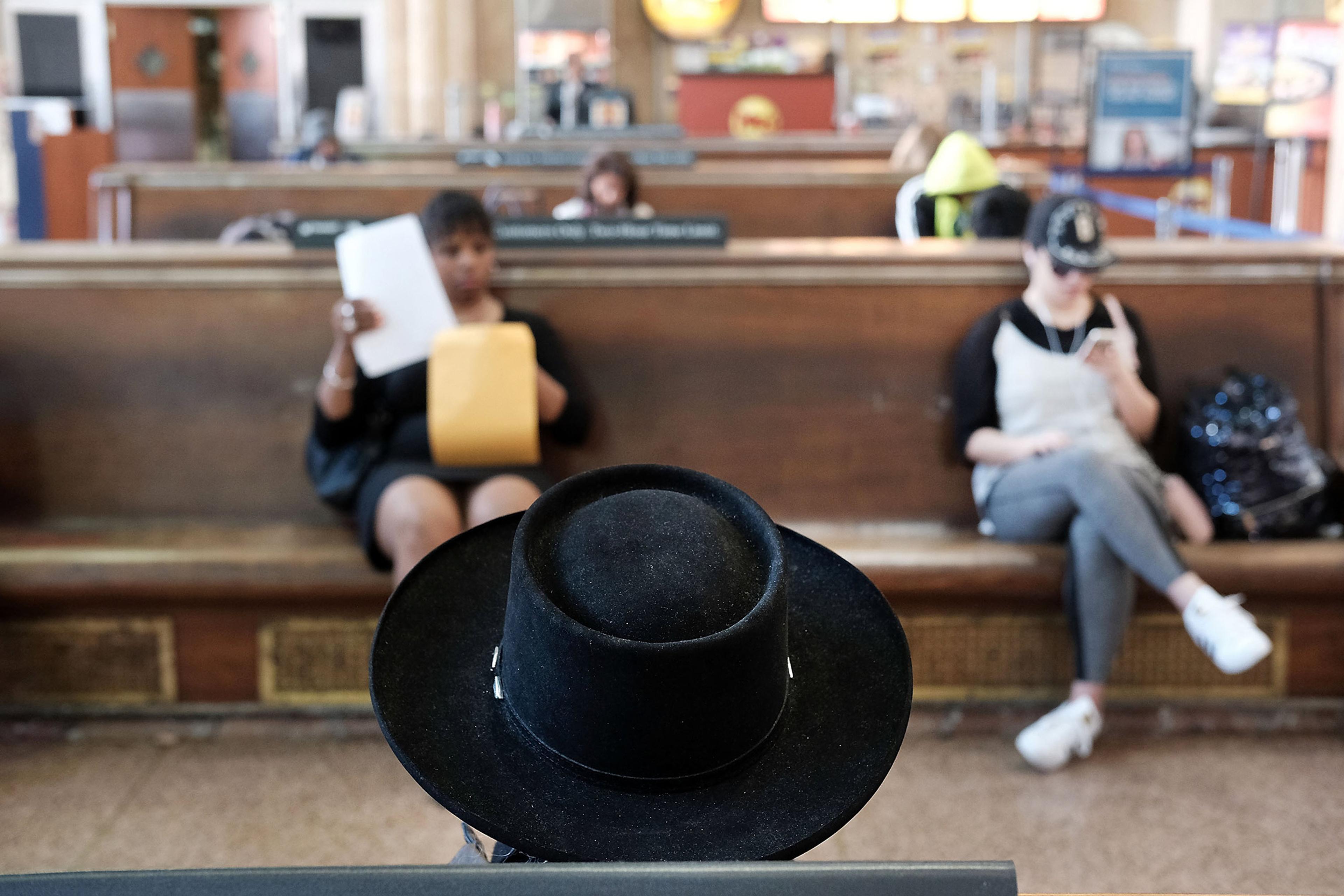 Photo of a waiting room with focus on a black hat. A woman reads papers and another looks at her phone in the background.