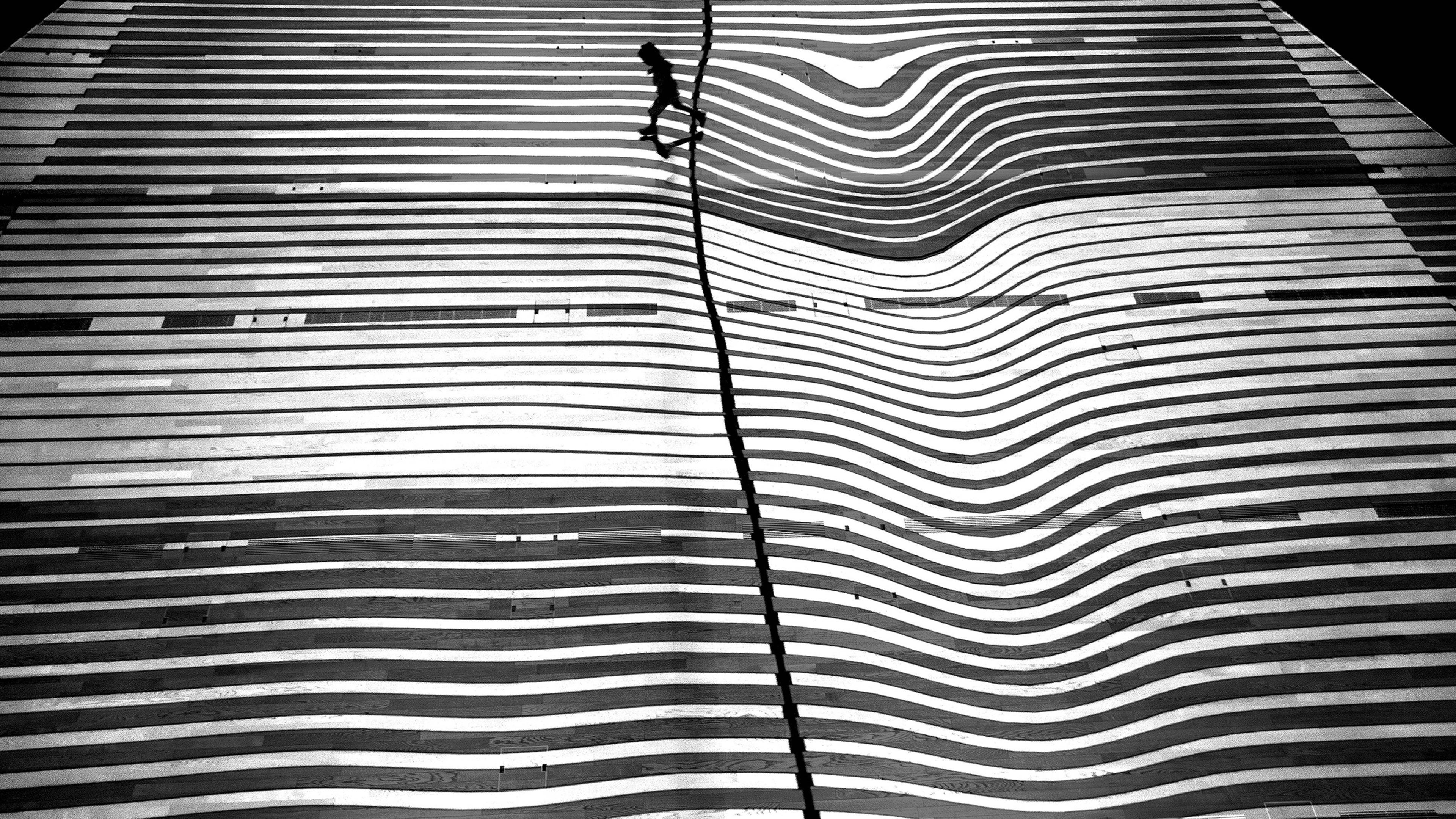Black and white photo of a person walking on a wavy striped surface creating an optical illusion.