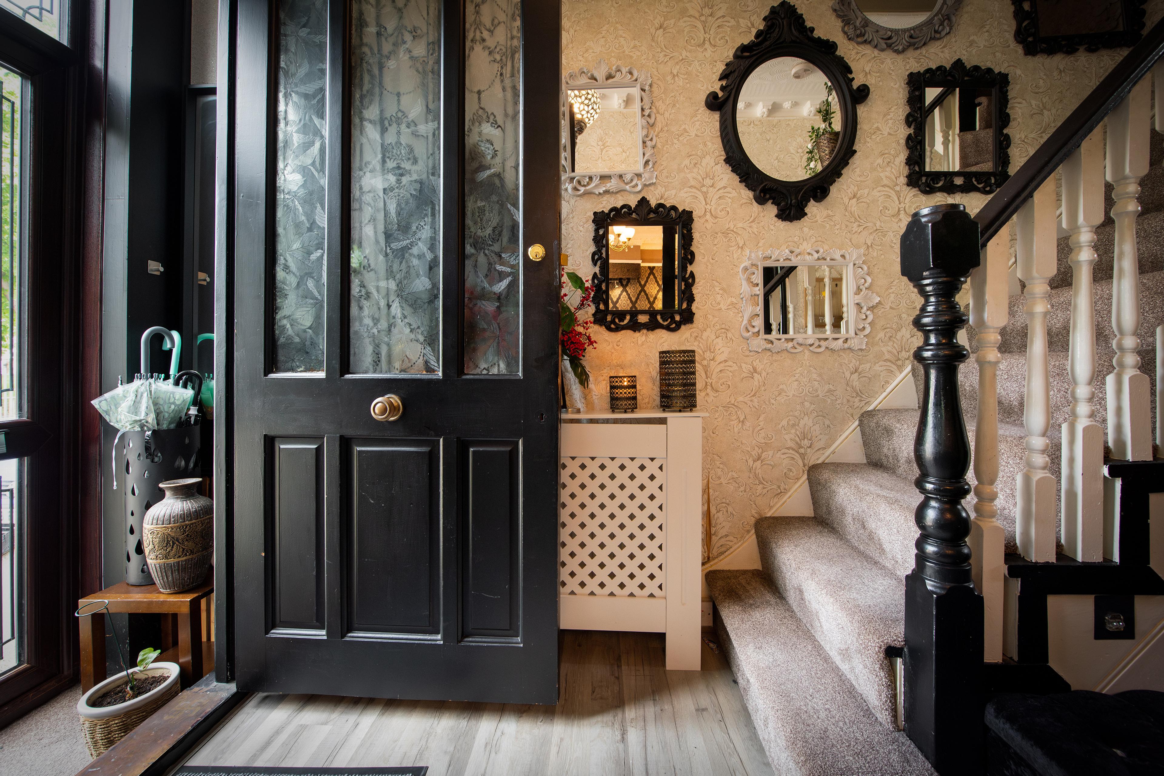 A home entrance with a black front door, mirrored wall, umbrella stand and carpeted stairs.